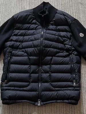 Svart pufferjacka från Moncler - Svart pufferjacka från Moncler med quiltad front och två dragkedjeförsedda fickor. Jackan har ribbad krage och ärmar i stickad material, samt Moncler-logga på ena ärmen. Perfekt för dig som vill ha en clean och stilren look. Skriv för mer bilder frågor eller prisförslag så löser vi nåt gött tsm 