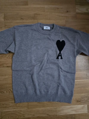 Grå stickad tröja Ami Paris - Grå stickad tröja med svart logga på bröstet från Ami Paris. I storlek M. Helt ny men taggen var helt uppriven så valde att klippa bort den.