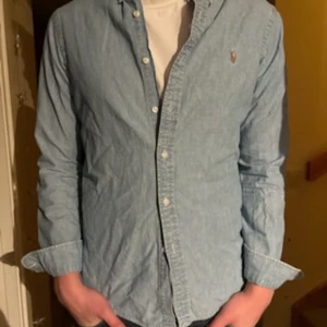 Ljusblå skjorta från Polo Ralph Lauren - Snygg ljusblå skjorta från Polo Ralph Lauren i slim fit-modell. Skjortan har klassisk krage, knappar framtill och ett litet broderat logomärke på bröstet. Perfekt för dig som gillar stilrena och tidlösa plagg.