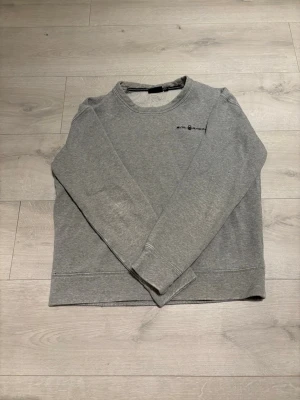 Grå Sail Racing sweatshirt - Säljer en grå sweatshirt från Sail Racing med diskret logga på bröstet och en liten detalj i nacken. Tröjan har rund hals, långa ärmar och är tillverkad i mjuk bomullsmix. Perfekt för chill dagar och enkel att matcha med jeans eller joggers.
