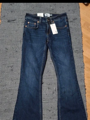 jeans  - Snygga bootcut jeans i mörkblå tvätt med låg midja och kort längd. Klassisk femficksdesign och kontrastsömmar. Perfekta för dig som gillar en retro vibe och vill ha ett par jeans som sitter tajt upptill och släpper vid benen.