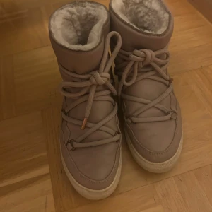 Rosa skor från Inuikii - Säljer ett par ljusrosa skor från Inuikii med mjukt foder och snörning framtill. Skorna har rund tå, platt sula och är tillverkade i skinn med syntetisk päls på insidan. Perfekta för kalla dagar när du vill hålla dig varm och snygg.