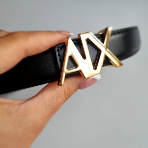 Svart skärp från Armani Exchange - Snyggt svart bälte från Armani Exchange i skinn med en fet guldfärgad AX-logga som spänne. Bältet har stilrena sömmar och flera hål för justering. Perfekt accessoar för att lyfta din outfit med en lyxig touch. 110cm 