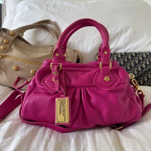 Rosa Q Classic Baby Groove väska! - Snyggaste rosa handväskan i äkta läder från Marc by Marc Jacobs. Den ikoniska modellen Q Classic Baby Groove! En populär och eftertraktad vintagemodell med gulddetaljer och dubbla handtag. Långa bandet finns. Väskan är i nyskick. Lädret är helt utan repor eller hål.  Det här är en tidlös modell som inte längre finns att köpa, vilket gör den extra eftertraktad. Perfekt för dig som vill ha en stilren tidlös väska med riktigt bra andrahandsvärde. Skriv för mer info eller bilder 🤍
