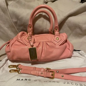 Rosa handväska från Marc Jacobs - 30x20x10 cm  Väskan är i nästan nyskick, helt utan skador. Den säljs med axelrem och dust bag. Jag hade egentligen tänkt ge den som en födelsedagspresent till en vän. 
