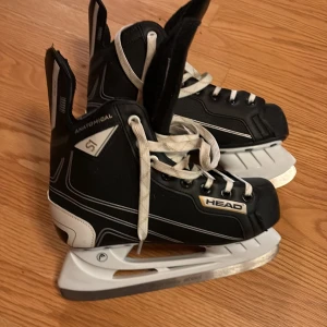 Svarta hockeyskridskor från Head, 38 - Säljer ett par svarta hockeyskridskor från Head i storlek 38. De har vita snören, robust svart och vit design samt anatomisk passform. Metallblad och vadderad plös för extra komfort. Inga defekter knappt använda 
