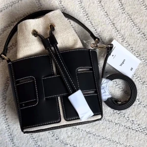 Svart och beige axelväska från H&M - Trendig axelväska från H&M i svart och beige med kontrasterande vita sömmar. Väskan har både handtag och justerbar axelrem samt snygga guldfärgade detaljer. Tillverkad i veganskt syntetmaterial och canvas, med smart snörning upptill.