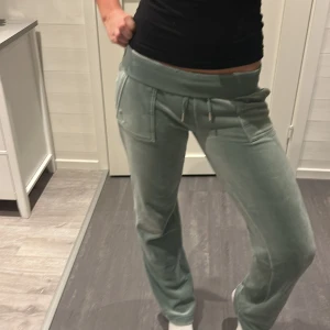Juicy Couture ljusgröna mjukisbyxor - Ljusgröna mjukisbyxor från Juicy Couture i mjuk velour med bred resår i midjan och snörning. Byxorna har raka ben, fickor fram och bak med knappdetalj samt broderad JC-logga vid fickan. Perfekta för en chill och trendig look.