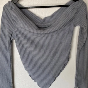 Grå ribbad topp från SHEIN - Säljer en grå ribbad långärmad topp från SHEIN med snygg omlottkrage och spetsig nederkant. Toppen har en figurnära passform och är tillverkad i mjuk polyesterblandning med stretch. Perfekt för dig som gillar trendiga och unika siluetter.