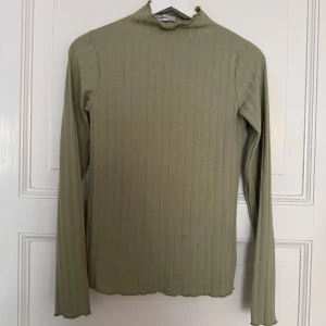 Ribbad grön polotröja från Chiquelle - Snygg ribbad polotröja i ljusgrön nyans från Chiquelle. Tröjan har lång ärm, smal passform och en liten ståkrage med råa kanter. Perfekt att styla med jeans eller kjol för en clean look. Värt att notera är att jag uppmärksammade en sminkfläck (bild 3), men jag tvättar bort den innan jag postar. 