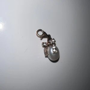 Thomas sabo pärla och rosett rosé - Supersött hängsmycke med en vit pärla och en glittrig rosett i silverfärg. Perfekt att fästa på ett halsband eller armband. Rosetten är dekorerad med små stenar som ger extra bling. Smidigt klolås i metall gör det enkelt att byta mellan olika smycken.