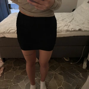 Kjol - Snygg svart kortkjol med tight passform och lätt rynkade sidor. Kjolen är enkel och stilren, perfekt för dig som gillar minimalistisk look. 