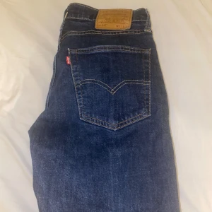 Levi's 512 mörkblå jeans W31 L32 - Mörkblå Levi's 512 jeans med klassisk femficksdesign och snygga kontrastsömmar. Modellen har en smal passform och är tillverkad i slitstarkt denimtyg. Perfekta för dig som gillar en stilren och tidlös look.