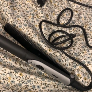 Voltage Plattång - Snygg och funktionell plattång från Voltage med enkel on/off-knapp. Svart och silver design, sladd i gott skick. Inga synliga defekter eller större slitage, redo att användas för att skapa släta och glansiga frisyrer.