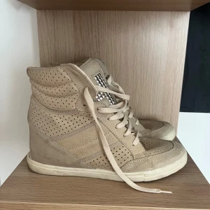 Sneakers med kilklack  - Snygga beige sneakers med kilklack i mockaliknande material. Använda typ 4 grg. Skorna har snörning och coola silvriga nitar i korsmönster på plösen.  Inte äkta Isabelle marant skor! 
