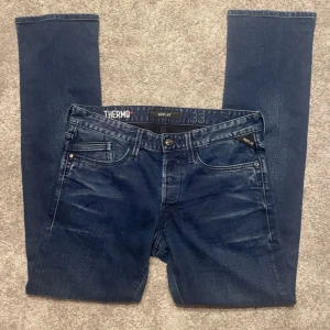 Blå Replay  - Säljer ett par mörkblå Replay jeans i straight fit. Klassisk femficksmodell med snygga slitningar och detaljerade bakfickor. Jeansen är tillverkade i ett värmande material och har normal passform. Perfekta för dig som vill ha stilrena och bekväma jeans.