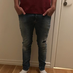 Blå slitna slimfit jeans från diesel - Säljer ett par blå slimfit jeans med slitningar från diesel. Jeansen har klassisk femficksdesign, knappgylf och en tight passform som sitter snyggt längs benen. Perfekta för dig som gillar en lite grisch stil.