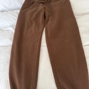 Bruna mjukisbyxor från NA-KD XXS - Mysiga bruna mjukisbyxor från NA-KD i storlek XXS. Byxorna har resår i midjan med snörning och är tillverkade i ett mjukt material som passar perfekt för chill dagar. Enkel och stilren design utan mönster eller detaljer.