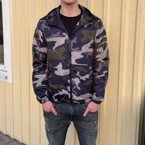 Camouflage vindjacka  - Säljer en snygg vind/höstjacka från Lindfors i mörk camouflage med dragkedja och huva. Perfekt för de kyligare vädret nu efter sommaren, storlek XS sitter som S samt att jackan är helt nyoch inplastade för 299 kr✅