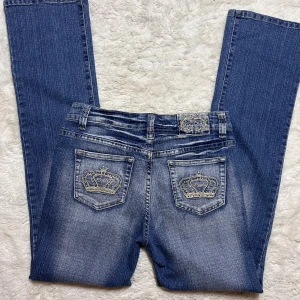  jeans med kronor på bakfickorna vintage 2000s y2k - Vintage jeans med coola detaljer och snygg wash. Uppskattad  storlek ungefär w29. Innerbenslängd: 80 midjemått: 38 stretch till 42. Midwaist & straight/lätt bootcut passform. Köp sker via köp nu, jag postar inom 24h, kvar tills markerad såld 