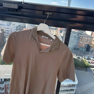 Beige pikétröja från Bläck - Säljer en stilren beige pikétröja från Bläck i storlek S. Tröjan har klassisk krage och korta ärmar, perfekt för en clean och avslappnad look. Tillverkad i mjuk bomull som känns skön mot huden.