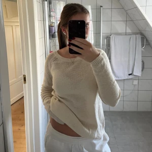 Krämvit stickad tröja med rosett - Superfin krämvit stickad tröja med lång ärm och snygg öppen rygg med svart rosett. Tröjan har en rund halsringning och diskreta hålstickade detaljer längs axlarna🤍strl S/M