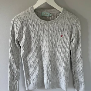 Ljusgrå morris kabelstickad tröja  - Kabelstickad ljusgrå tröja från Morris Lady i 100% pima bomull. Tröjan har rund halsringning, lång ärm och en broderad röd logga på bröstet. Perfekt för dig som gillar klassisk och stilren look. Passar till tjejer och är i dam storlek S. Tveka inte på att höra av dig vid minsta lilla fråga!🤩
