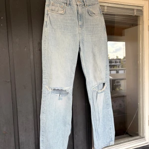 Ljusblå ripped straight jeans - Säljer ett par ljusblå jeans med raka ben och slitna hål över knäna. Mid/hög midja och snyggt avslappnad passform. 