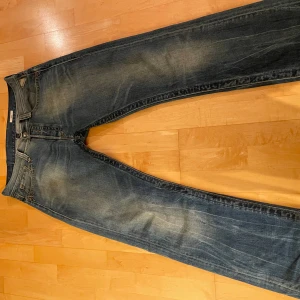 Blå jeans Replay - Säljer ett par klassiska blå jeans från Replay med snygga slitningar och kontrastsömmar. Modellen har raka ben och normal passform, fem fickor och tydlig logga bak. Perfekt för dig som gillar en tidlös jeanslook.