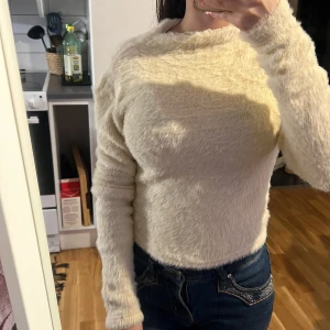 Beige fluffig tröja från Gina Tricot - Supermjuk och fluffig beige tröja från Gina Tricot i storlek XS. Tröjan har lång ärm och är tillverkad i ett stickat material med pälsliknande yta som ger en cozy vibe. Perfekt för dig som gillar en enkel men ändå mysig stil.