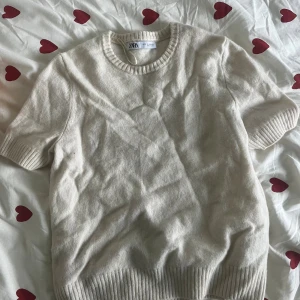 Beige stickad tröja från Zara - Beige stickad tröja från Zara med korta ärmar och rund halsringning. Tröjan har ribbade muddar vid ärmslut och nederkant, vilket ger en snygg och enkel look. Perfekt för lager-på-lager och passar till många olika stilar.