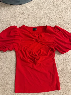 Röd puffärm topp från Gina Tricot - Säljer en snygg röd topp från Gina Tricot med puffiga korta ärmar och twistade detaljer framtill. Toppen har en figurnära passform. Perfekt för dig som vill sticka ut med färg. 