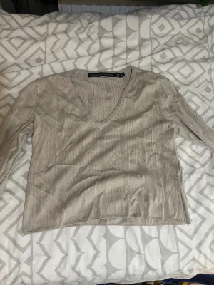 Beige ribbad stickad tröja  - Snygg beige stickad tröja från Lager 157 i storlek XL. Tröjan har ribbad struktur, v-ringad hals och långa ärmar. Perfekt för dig som gillar enkel och stilren design med en chill vibe.