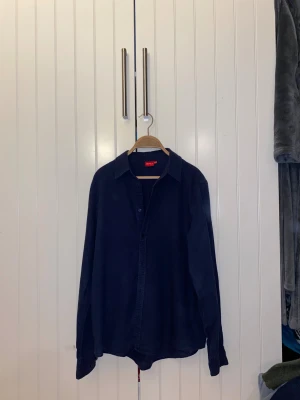 Mörkblå linneskjorta  - Snygg mörkblå linneskjorta från RYVLS med klassisk krage och knappar framtill. Skjortan har lång ärm och är gjord i mjuk bomull som känns skön mot huden. Perfekt för dig som gillar stilrena och enkla plagg med en chill vibe. Storleken är 170/176 men passar bra som XS/S. Tveka inte på att höra av dig vid minsta fundering, priset är inte hugget i sten😉