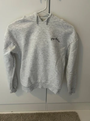 Grå hoodie med tryck från Gina Tricot - Snygg ljusgrå hoodie från Gina Tricot med svart tryck 'Ma chérie' fram och stort hjärta med pil på ryggen. Mjuk insida, huva med snörning och ribbade muddar. Perfekt för chill dagar och streetstyle.