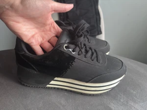 Svarta sneakers Calvin Klein EU 38 - Svarta sneakers från Calvin Klein med coola vita ränder på den tjocka plattformssulan. Skorna har snörning, rund tå och är tillverkade i syntetmaterial. Perfekt för dig som gillar chunky stil och vill ha något som sticker ut.