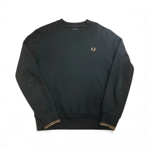 Blå  sweatshirt från Fred Perry -  sweatshirt från Fred Perry med guldigt broderat logomärke på bröstet. Tröjan har rund hals, ribbade muddar med guldfärgade ränder och är långärmad. Materialet är mjuk bomull och passformen är normal. Perfekt för dig som gillar stilrena och klassiska plagg.