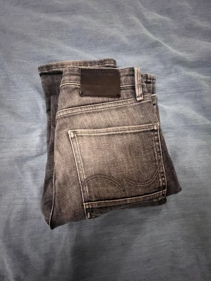 Slim Straight Fit grå jeans - Slim Straight Fit jeans i en snygg grå tvätt med slitningar. Klassisk femficksmodell, raka ben och låg midja. Jeansen har metallknapp och dragkedja fram, samt detaljerade sömmar på bakfickorna. Perfekt för dig som gillar en clean och stilren look. Öppen till prutning. Bra skick. 