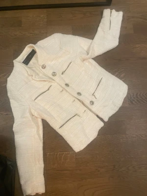 Vit kavajjacka från Zara med dragkedjor - Snygg vit kavajjacka från Zara med strukturerat tyg och silvriga knappar. Jackan har flera dekorativa dragkedjor framtill och på ärmarna, vilket ger en cool och modern vibe. Perfekt för dig som gillar stilrena detaljer och vill sticka ut.