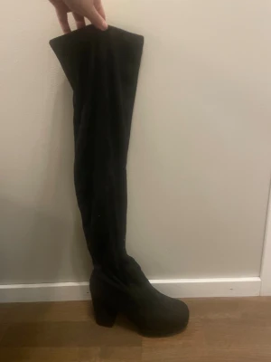 Svarta overknee stövlar med klack - Säljer ett par svarta overknee stövlar i mocka-look med chunky hög klack och rund tå. Snyggt höga och perfekta till kjol eller klänning. Plattformsula för extra komfort och stil.