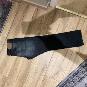  mörkblå jeans straight fit - Mörkblå  jeans med klassisk straight fit och snyggt slitna detaljer på låren. Jeansen har fem fickor, gylf med knappar och den ikoniska läderpatchen bak i midjan. Perfekta för dig som gillar en tidlös och avslappnad stil.
