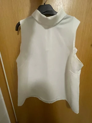 Vit ärmlös polotopp från Bik Bok - Säljer en stilren vit ärmlös polotopp från Bik Bok i storlek S. Toppen har en hög krage och en snygg dragkedja framtill som ger en modern touch. Perfekt att matcha med jeans eller kjol för en clean look.