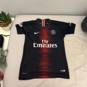 PSG Neymar Jr 10 matchtröja Nike - Säljer en icke äkta Paris Saint-Germain fotbollströja från Nike med Neymar Jr och nummer 10 på ryggen. Tröjan är mörkblå med röd och vit detalj framtill, kortärmad och tillverkad i lätt funktionsmaterial. Perfekt för dig som älskar PSG och Neymar.