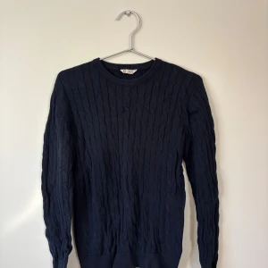  Kabelstickad tröja - 158/164 - Snygg mörkblå kabelstickad tröja från C i storlek 158/164. Tröjan har rund hals, långa ärmar och ett klassiskt kabelmönster. 
