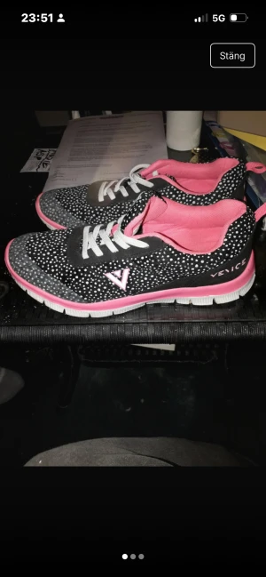 Svarta och rosa sneakers från Venice - Snygga sneakers från Venice med svart och vitt prickigt mönster, rosa detaljer och innersula. Skorna har vita snören, platt sula och grå partier framtill. Perfekta för dig som vill sticka ut med färg och mönster i vardagen.