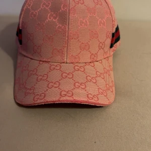 Rosa dubell G keps med fin mönster - Säljer en rosa keps med ikoniskt GG-monogram över hela kepsen. Kepsen har klassisk böjd skärm, justerbart spänne bak i rosa läder men dessutom gröna och röda signaturrand på sidan. Materialet är bomullscanvas med detaljer i läder. Kepsen är oanvänd. (priset är ej hugget i sten)