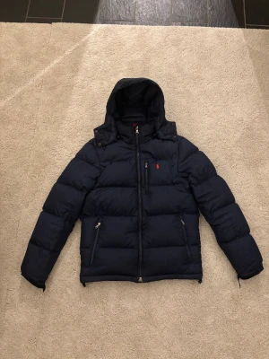 Ralph lauren vinterjacka - Tja! Säljer nu en snygg mörkblå dunjacka i storlek S från Polo Ralph Lauren med huva och dragkedja. Jackan är inköpt i slutet av förra vintern. Den har inga defekter och är i toppskick! Bara att höra av sig vid frågor och funderingar!