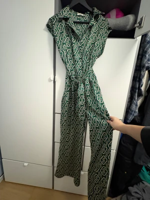 Grön mönstrad byxdress från MNG - Grön och vit byxdress från MNG med grafiskt mönster, knappar framtill och bälte i midjan. Långa, vida ben och kort ärm. Sval och mjuk känsla, perfekt för dig som gillar statement-plagg med cool retrovibe.