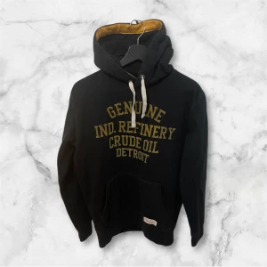 Svart hoodie från Petrol Industries - Svart hoodie från Petrol Industries med gul text på bröstet och kontrastfärgad insida i huvan. Tröjan har snörning vid huvan, stor magficka och långa ärmar. 