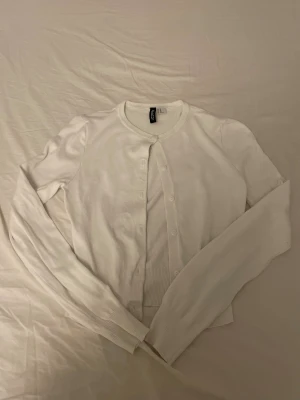 Vit kofta XS - Vit, klassisk kofta i storlek XS. Den har rund hals, långa ärmar och knappar framtill. Materialet är mjukt och känns som bomull, med ribbade muddar vid ärmslut och nederkant. Perfekt att slänga över en topp för en chill look.